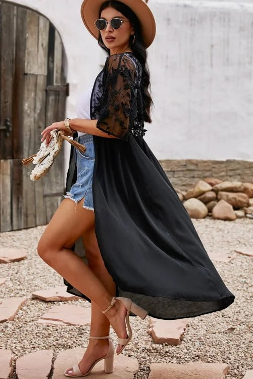 Woman in a black dress and straw hat standing on a pebbled surface with a rustic background.