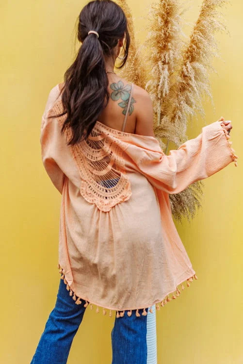Woman wearing a peach lace top with blue pants against a yellow background